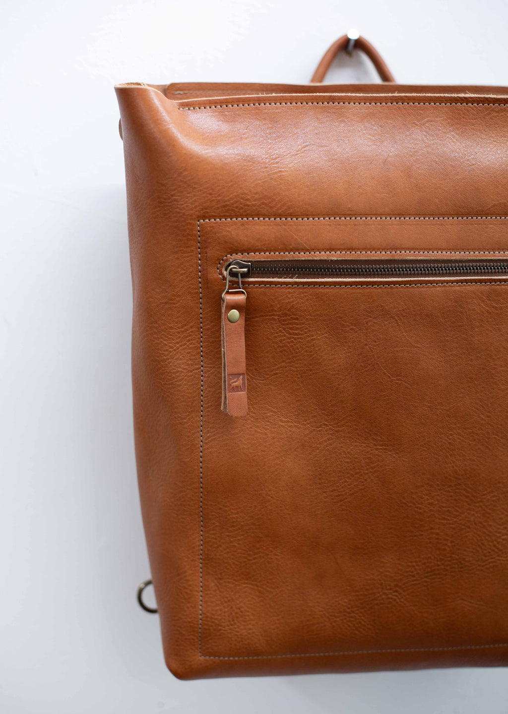 The leather bag / backpack is made with sustainable leather from hides from organically raised cattle. The leather has a visible grain and texture and is reddish brown. 