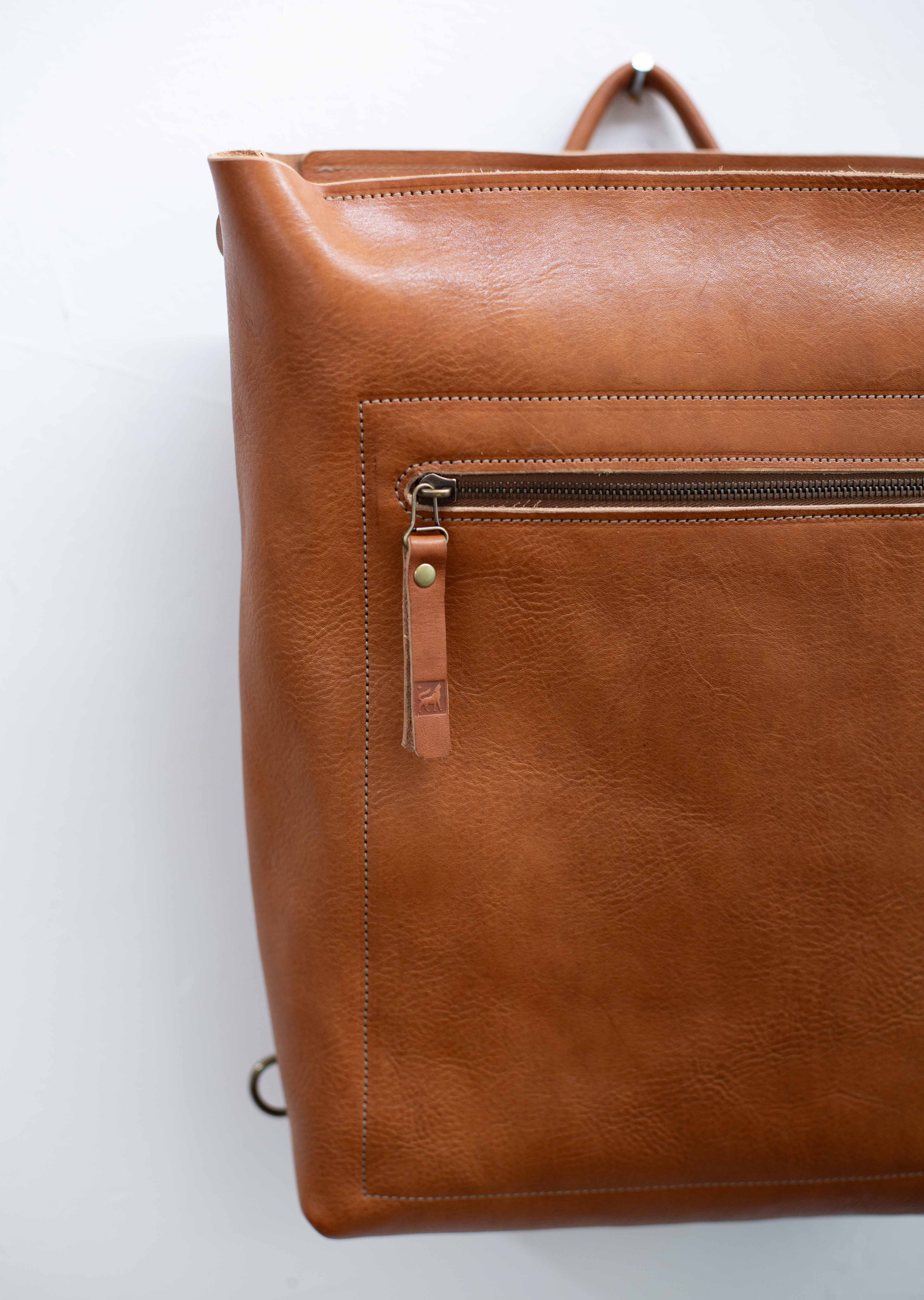 The leather bag / backpack is made with sustainable leather from hides from organically raised cattle. The leather has a visible grain and texture and is reddish brown. 
