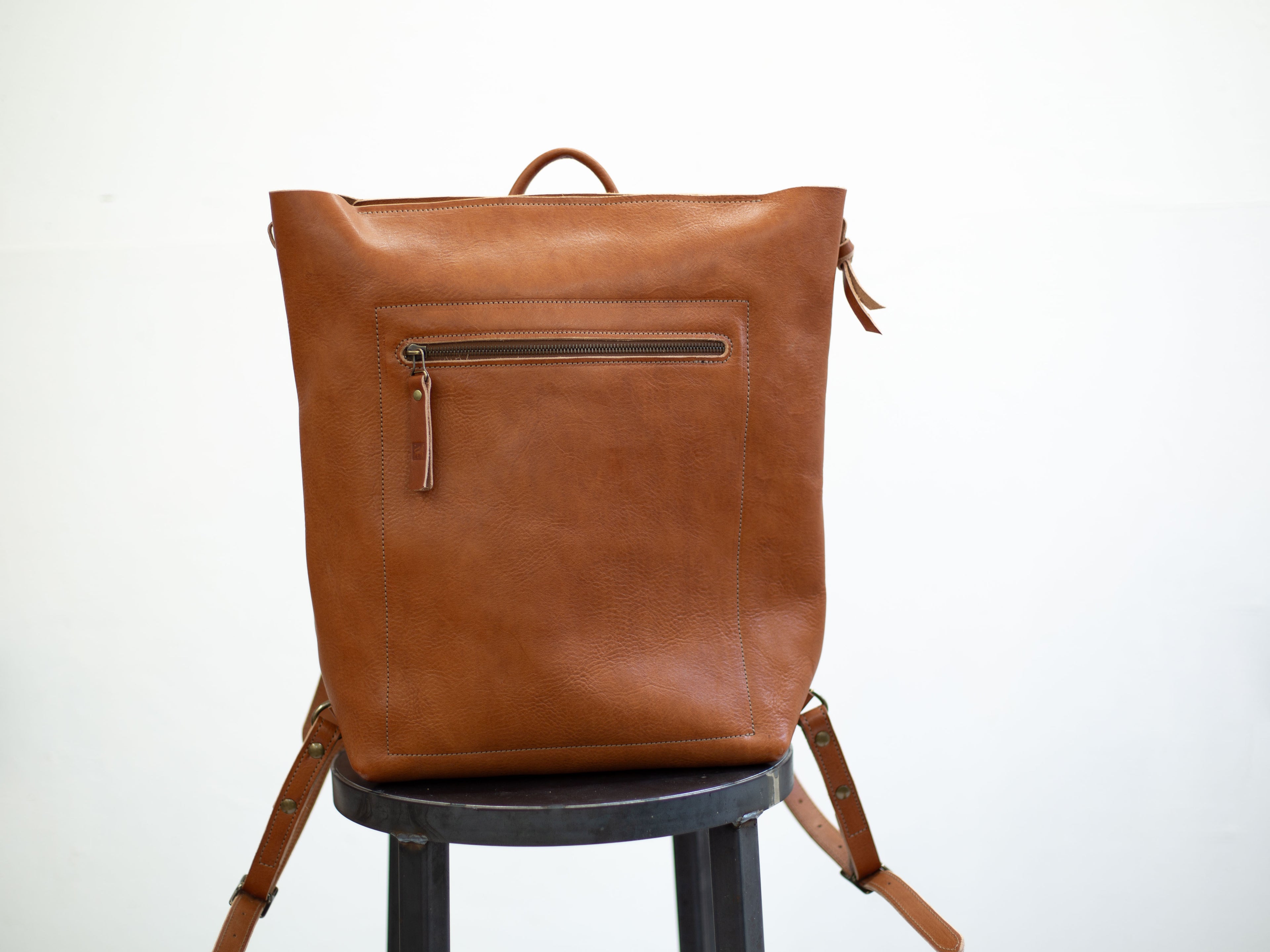 On the front the convertible leather backpack, made with sustainable organic leather, has a zipped front pocket for wallet, phone, etc. 