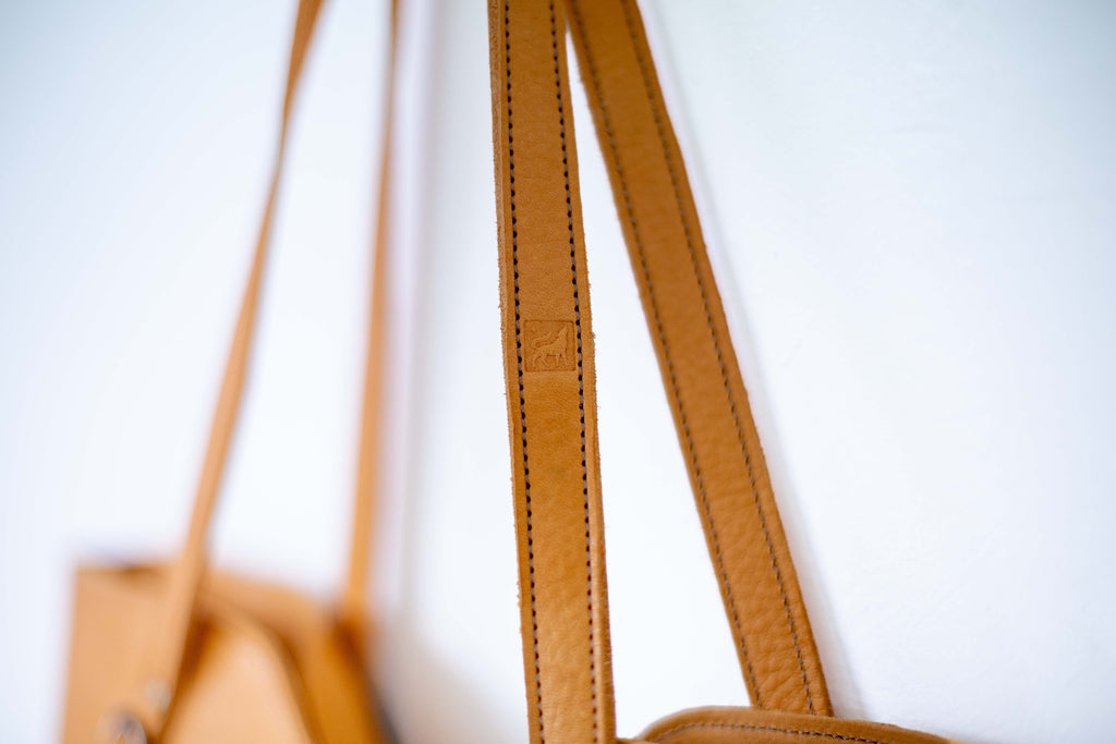 Close-up of the large beige leather bag to show the logo of White Wolf Leather Studio on the strap.