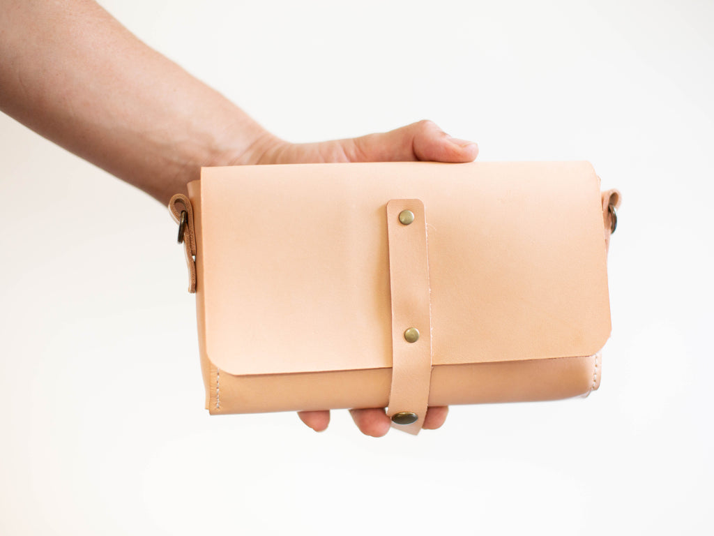 The small leather fanny pack is shown as size comparison to a hand