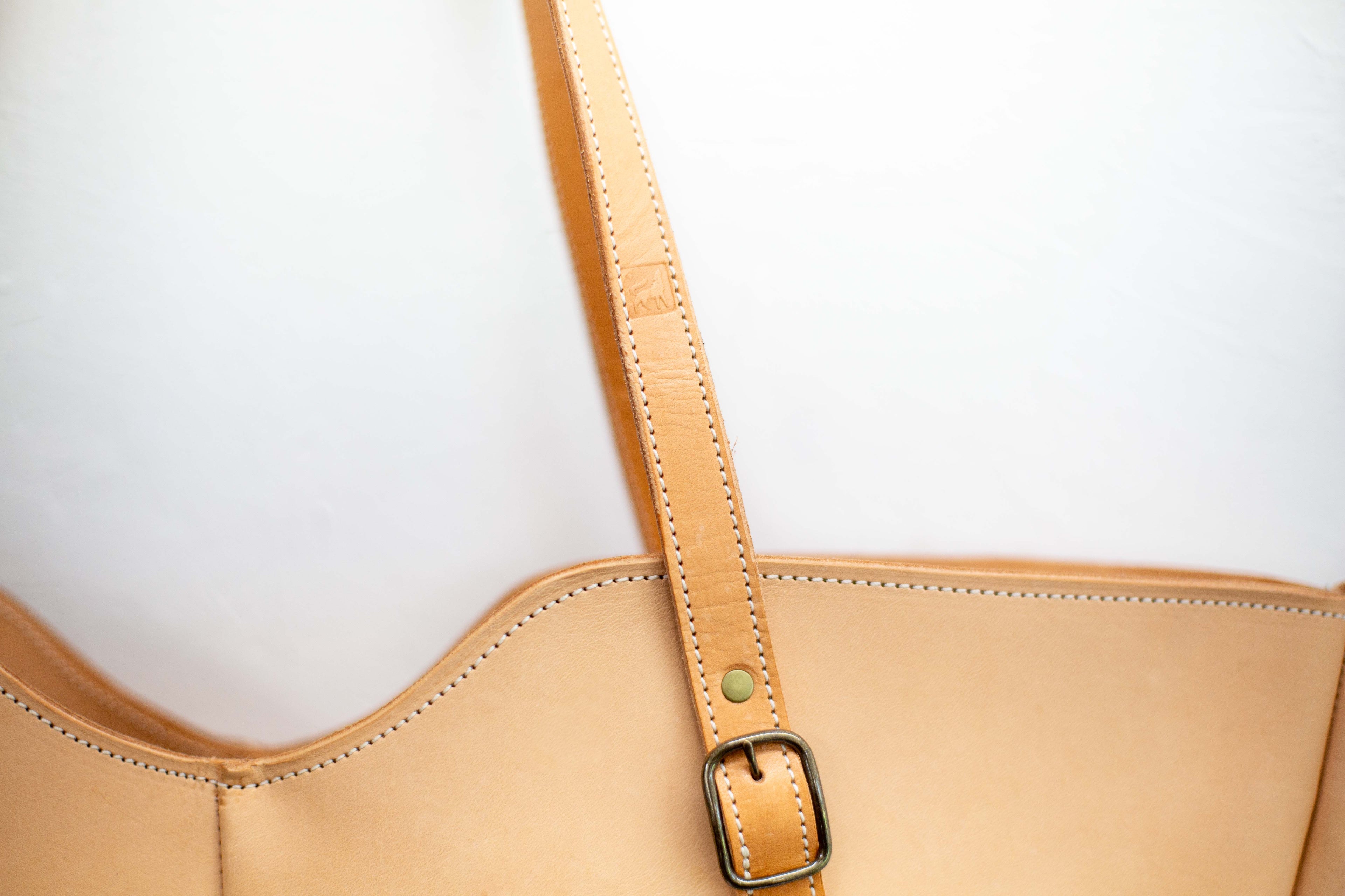 The strap of the sustainable leather bag shows the logo of White Wolf Leather Studio stamped in its strap. 