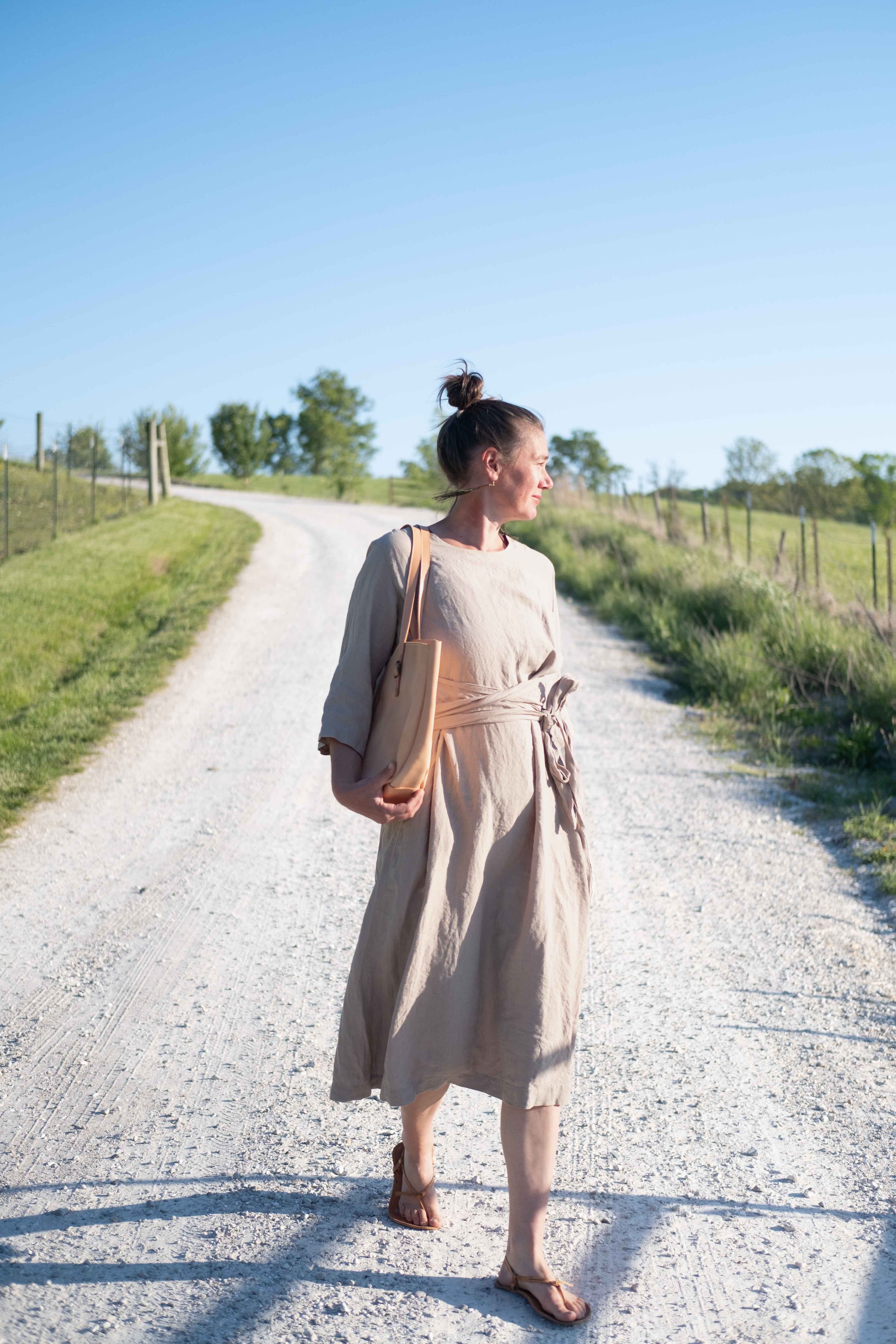 A woman is walking down a country road with the large leather tote bag over her shoulder.