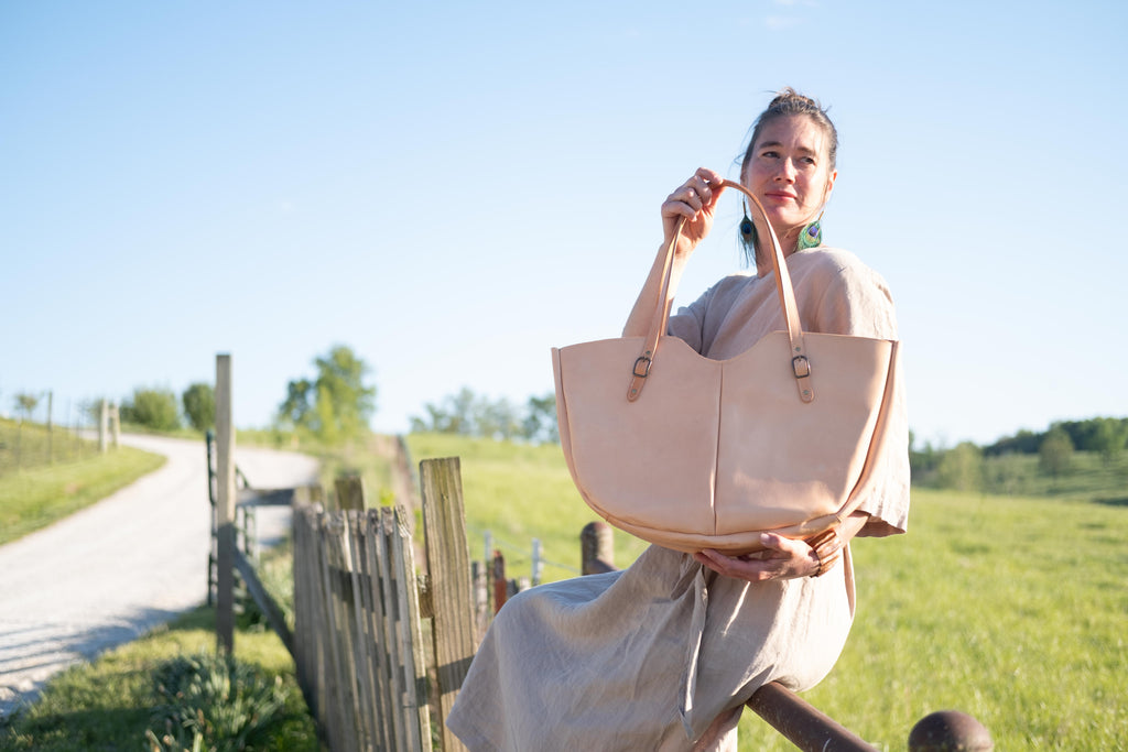 The large leather shoulder bag is being held in the camera on a sunny day in a country setting. 