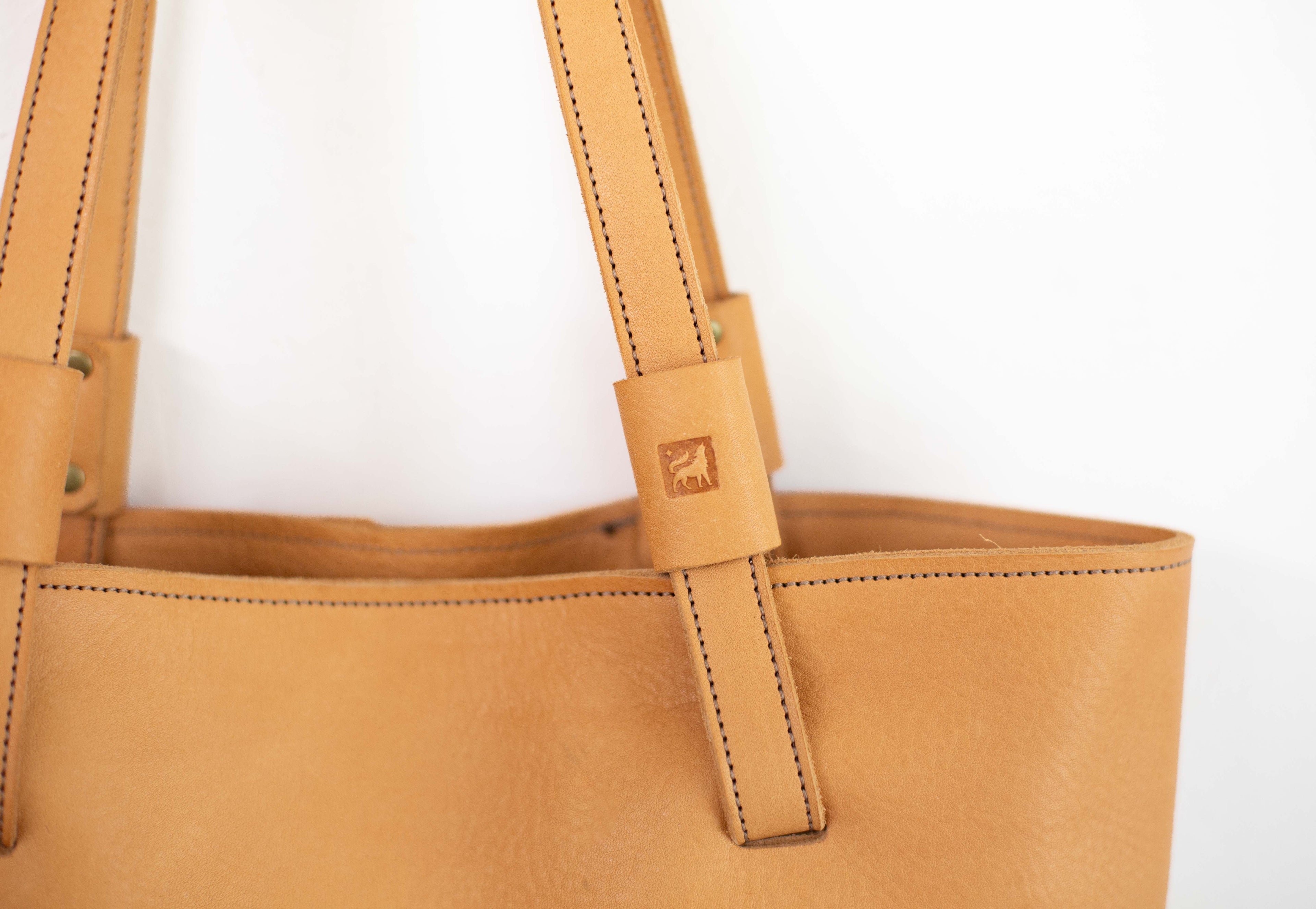 Close up of straps and White Wolf Leather Studio logo of the large leather bag. 