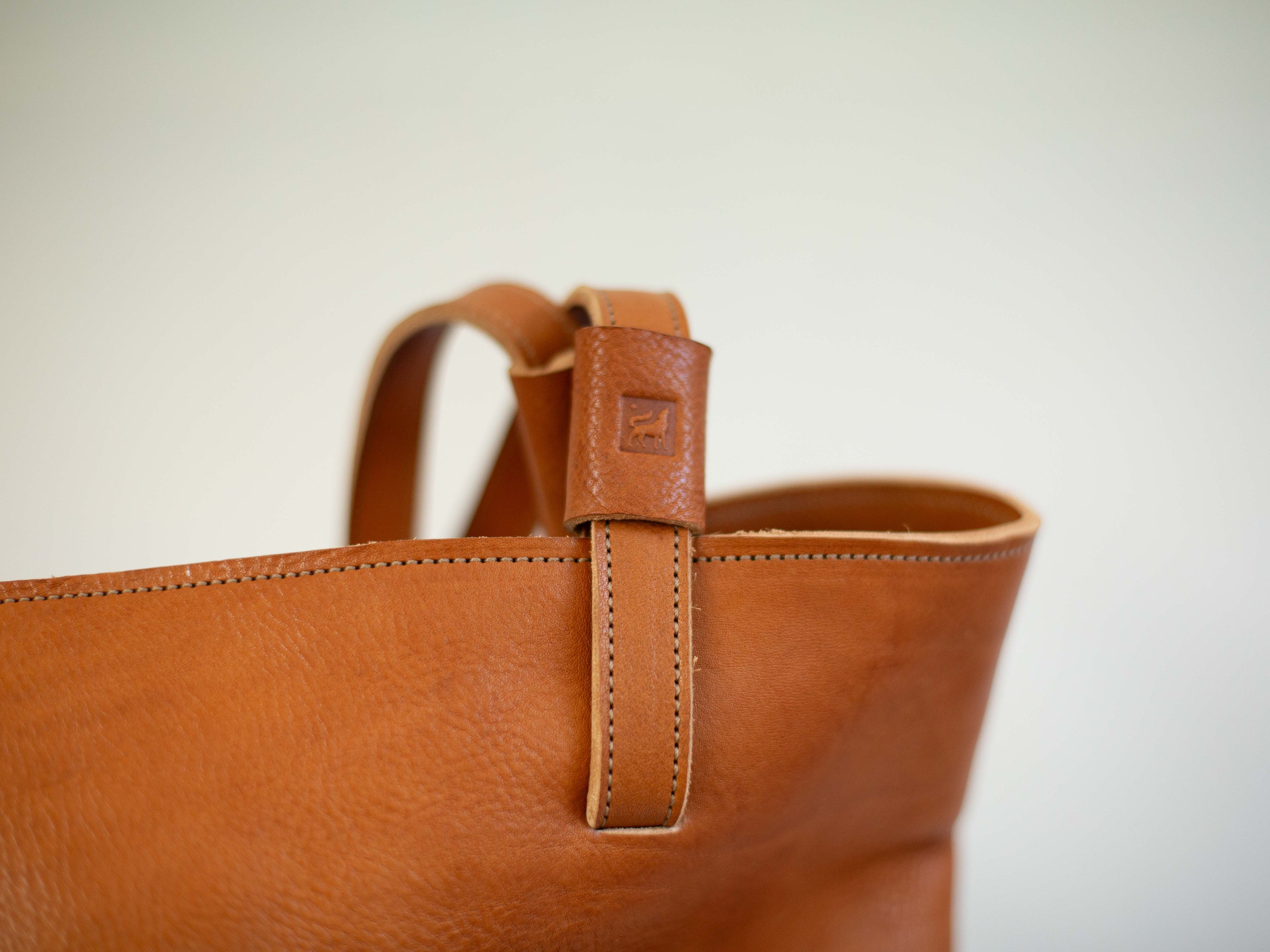 The logo of White Wolf Leather Studio is stamped into the shoulder strap of the organic leather tote bag. 