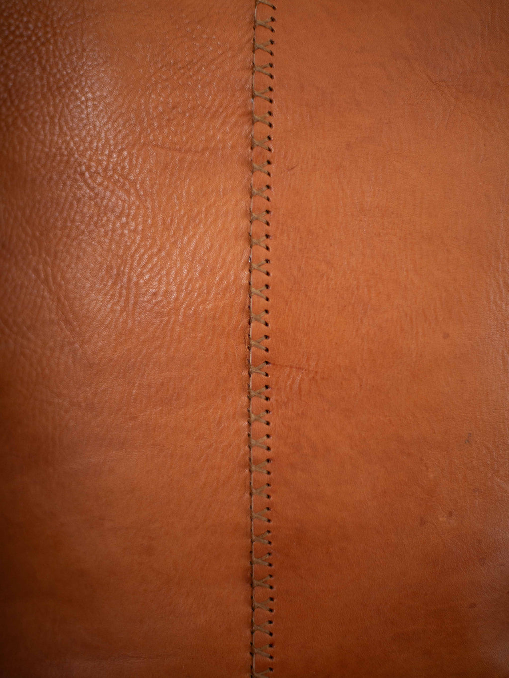 A close-up on the hand stitched seam on the back of the leather tote and the sustainable leather. 