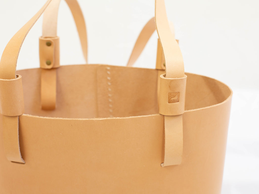 The close-up of the ethically made leather tote bag shows the straps and logo of White Wolf Leather Studio. 