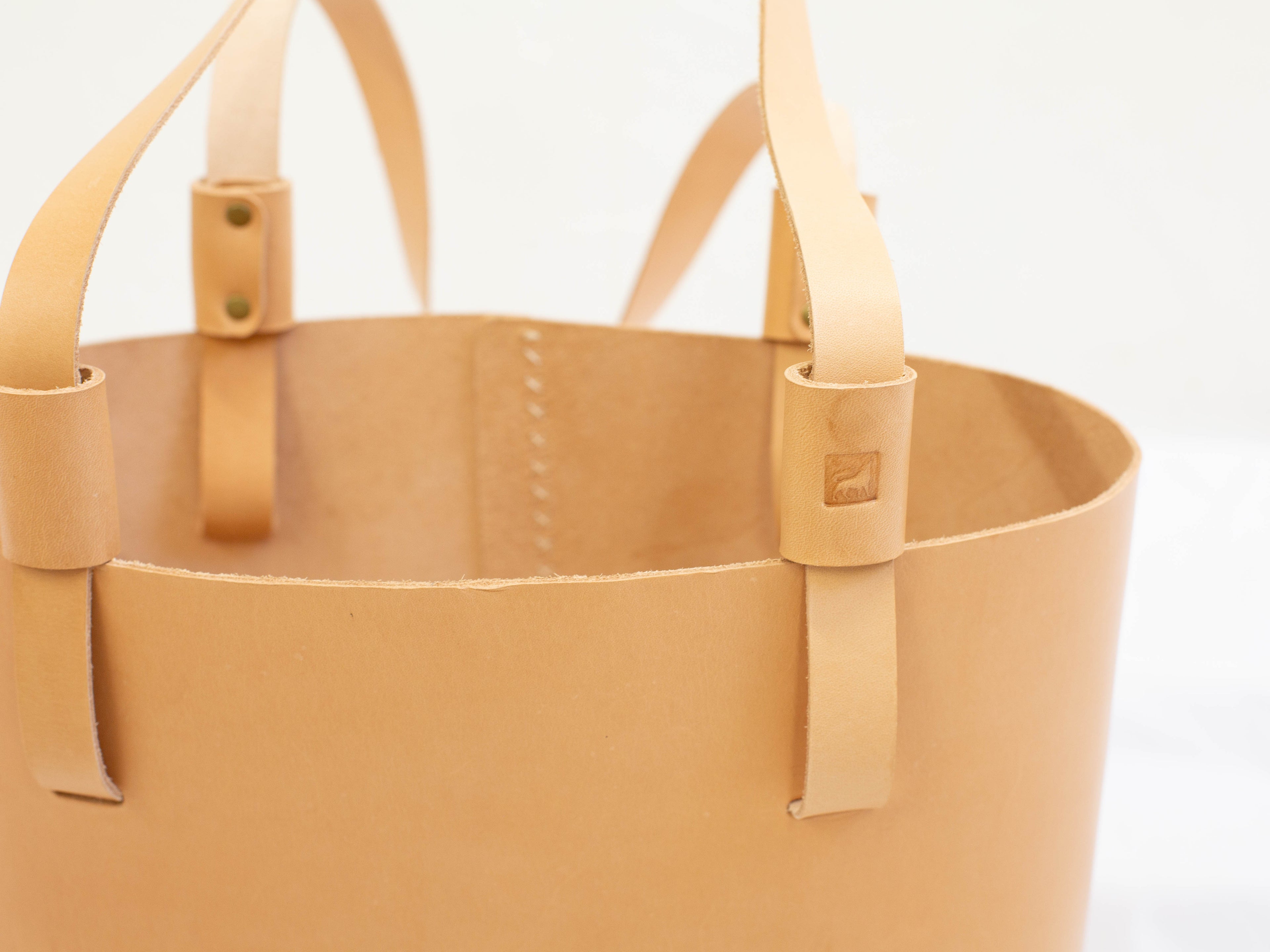 The close-up of the ethically made leather tote bag shows the straps and logo of White Wolf Leather Studio. 