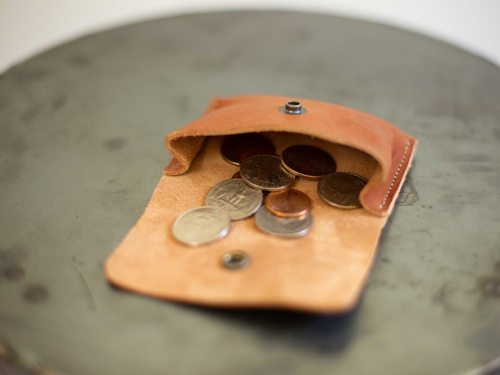 The small coin wallet made with sustainable leather is seen open, with coins, to see the capacity of the main compartment. 