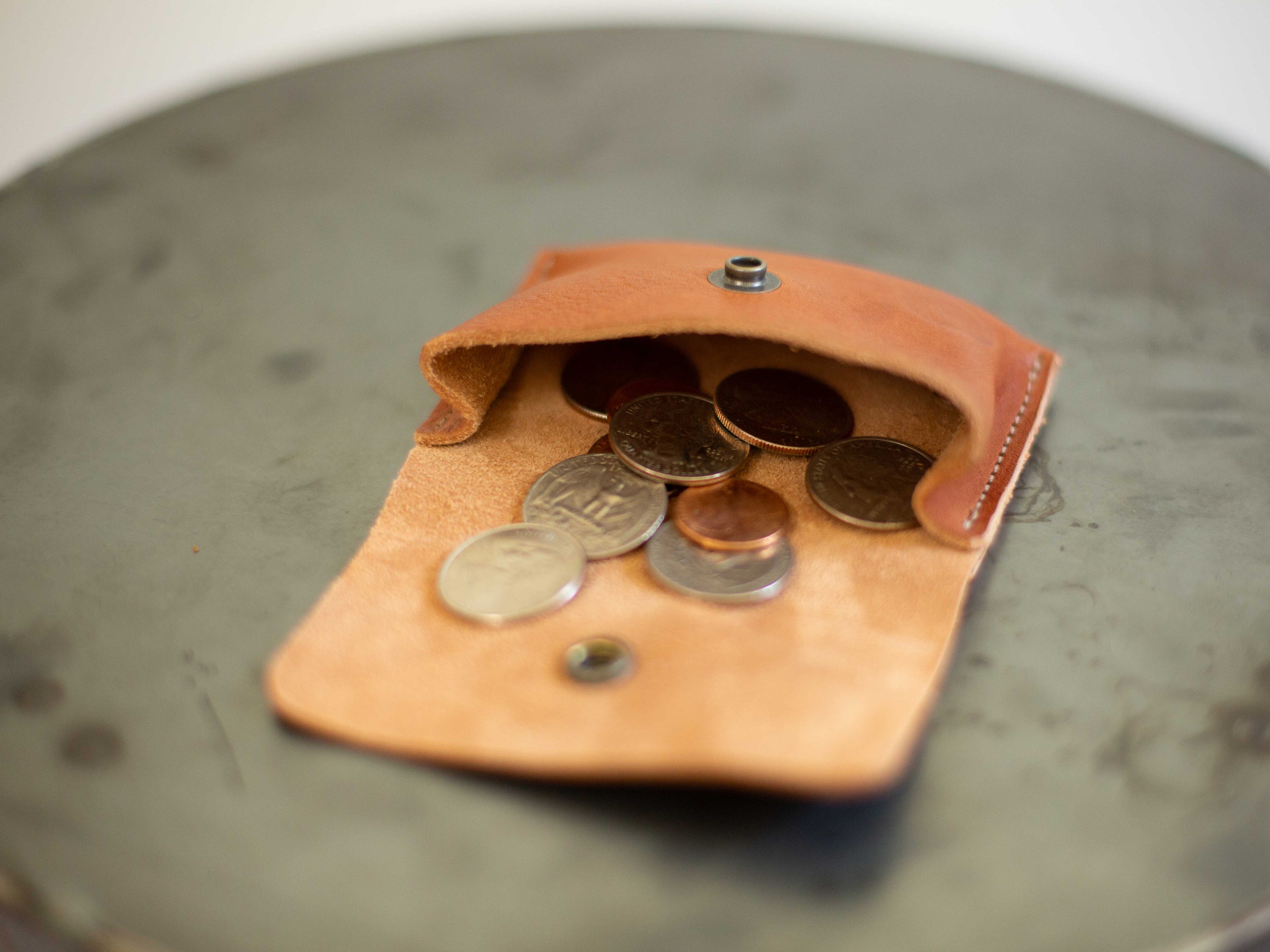 The small coin wallet made with sustainable leather is seen open, with coins, to see the capacity of the main compartment. 