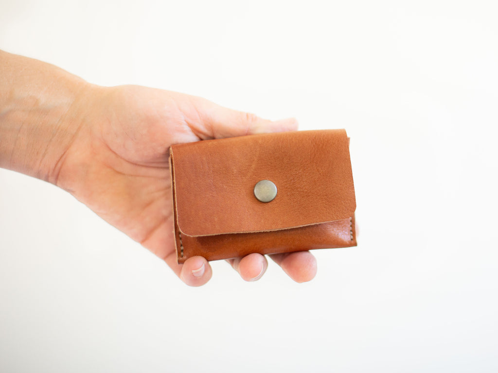 The small coin wallet is made with organic, sustainable reddish brown leather with visible grain and texture. 