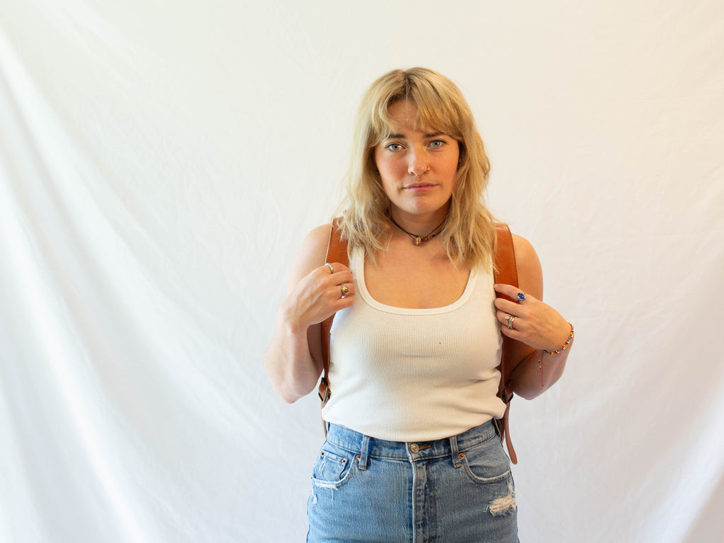 Front look at a model who is wearing the ethically made leather backpack, showing the straps of the backpack. 