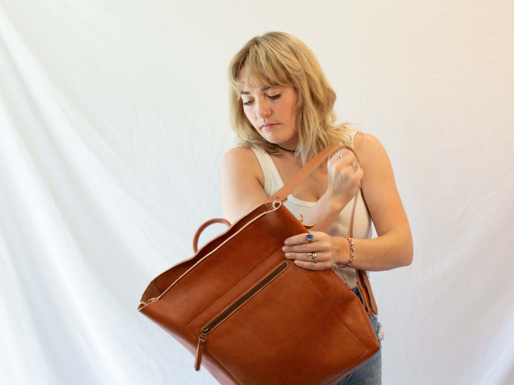 The medium sized leather backpack is closed with a zipper. The picture shows the model taking it of in order to convert it. 