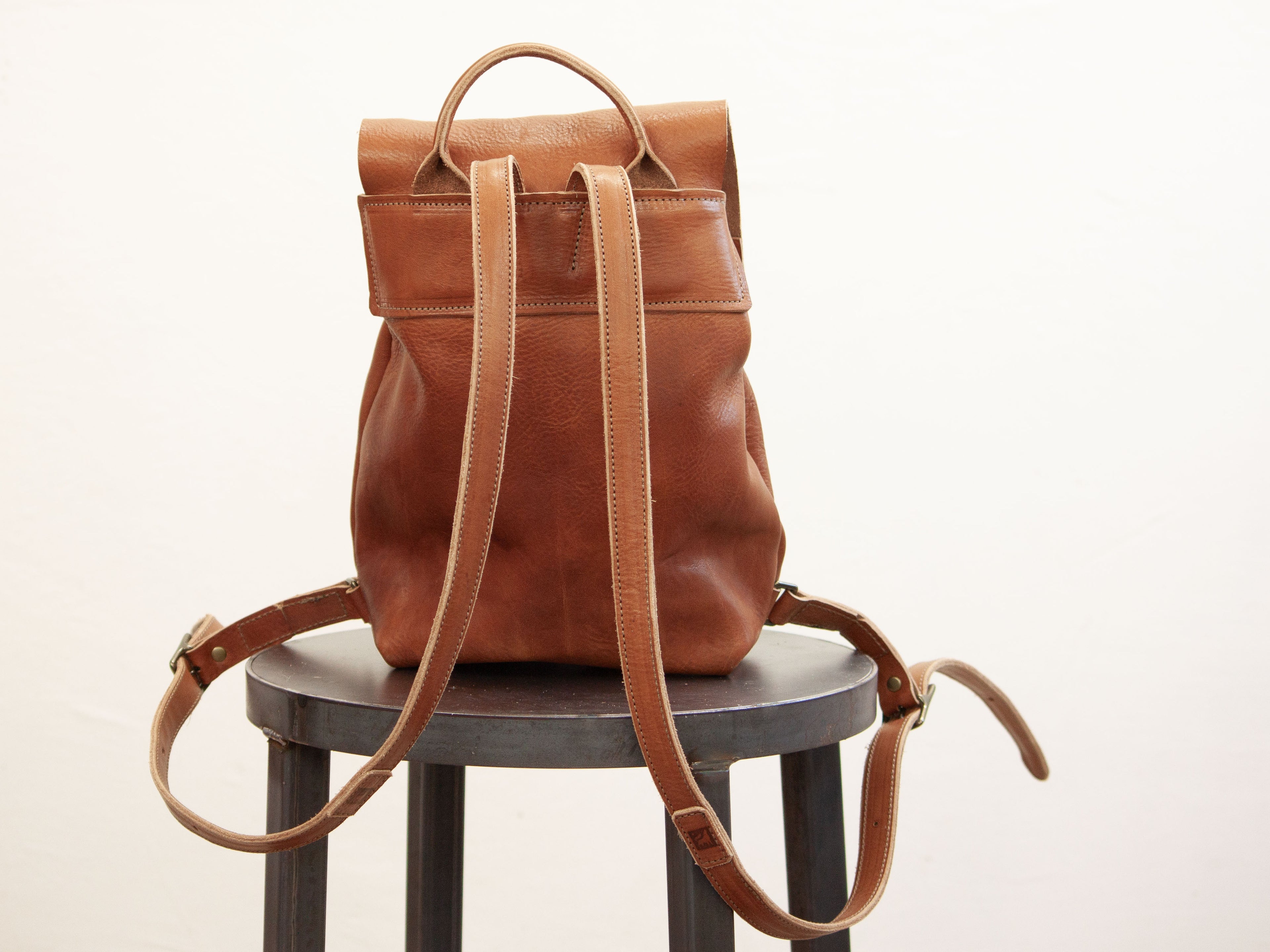 The back of the leather backpack is seen and shows the seams and handmade details. 