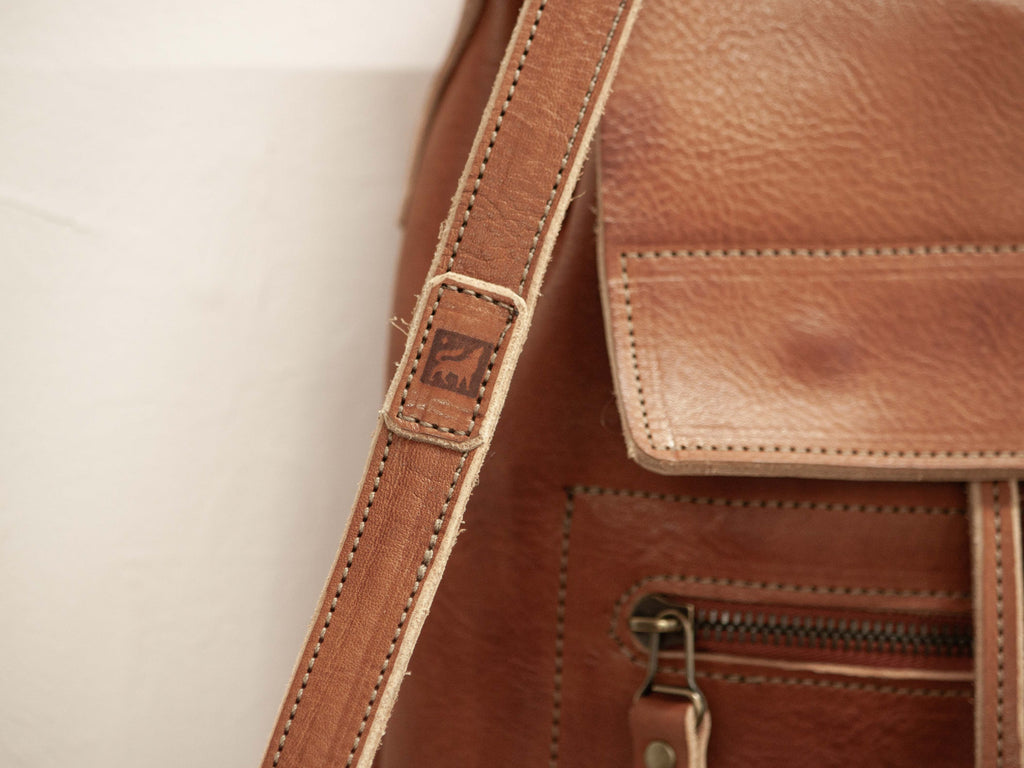 The branded logo of White Wolf Leather Studio - the brand that stands for quality handmade leather products with sustainably sourced leather - is sewn onto the backpack strap. 