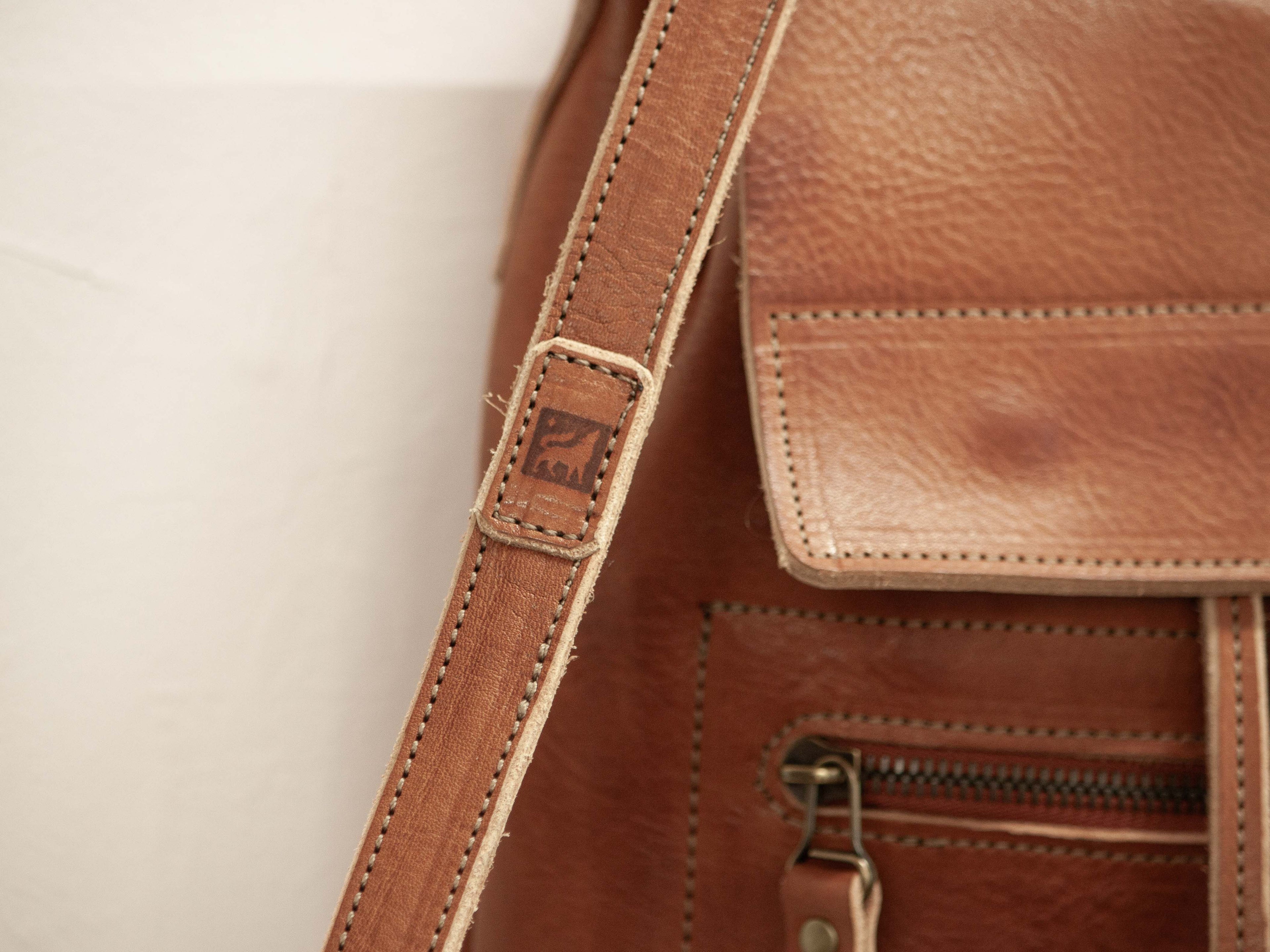 The branded logo of White Wolf Leather Studio - the brand that stands for quality handmade leather products with sustainably sourced leather - is sewn onto the backpack strap. 