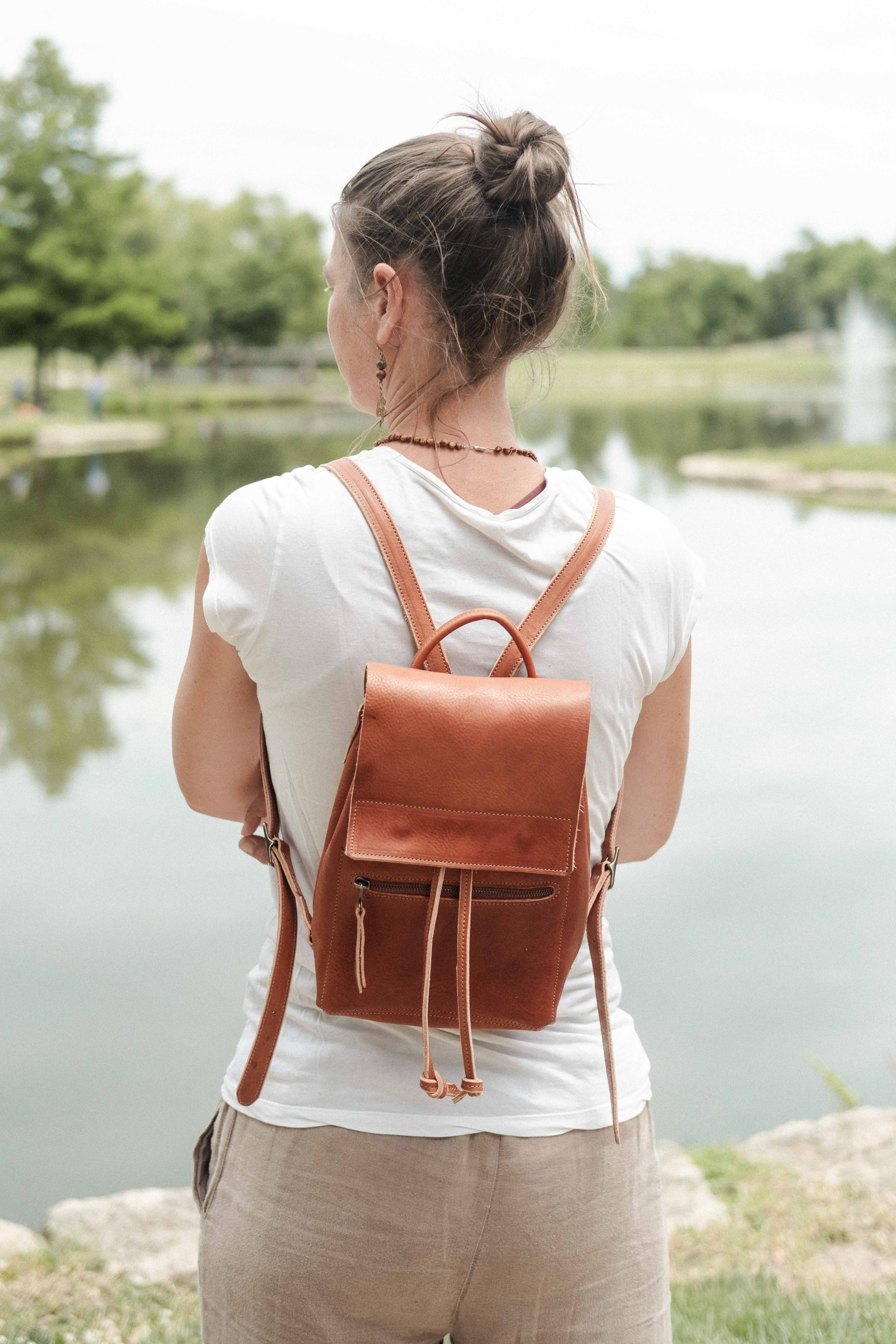 A woman is wearing the small leather drawstring backpack on a day trip in summer to the lake. 
