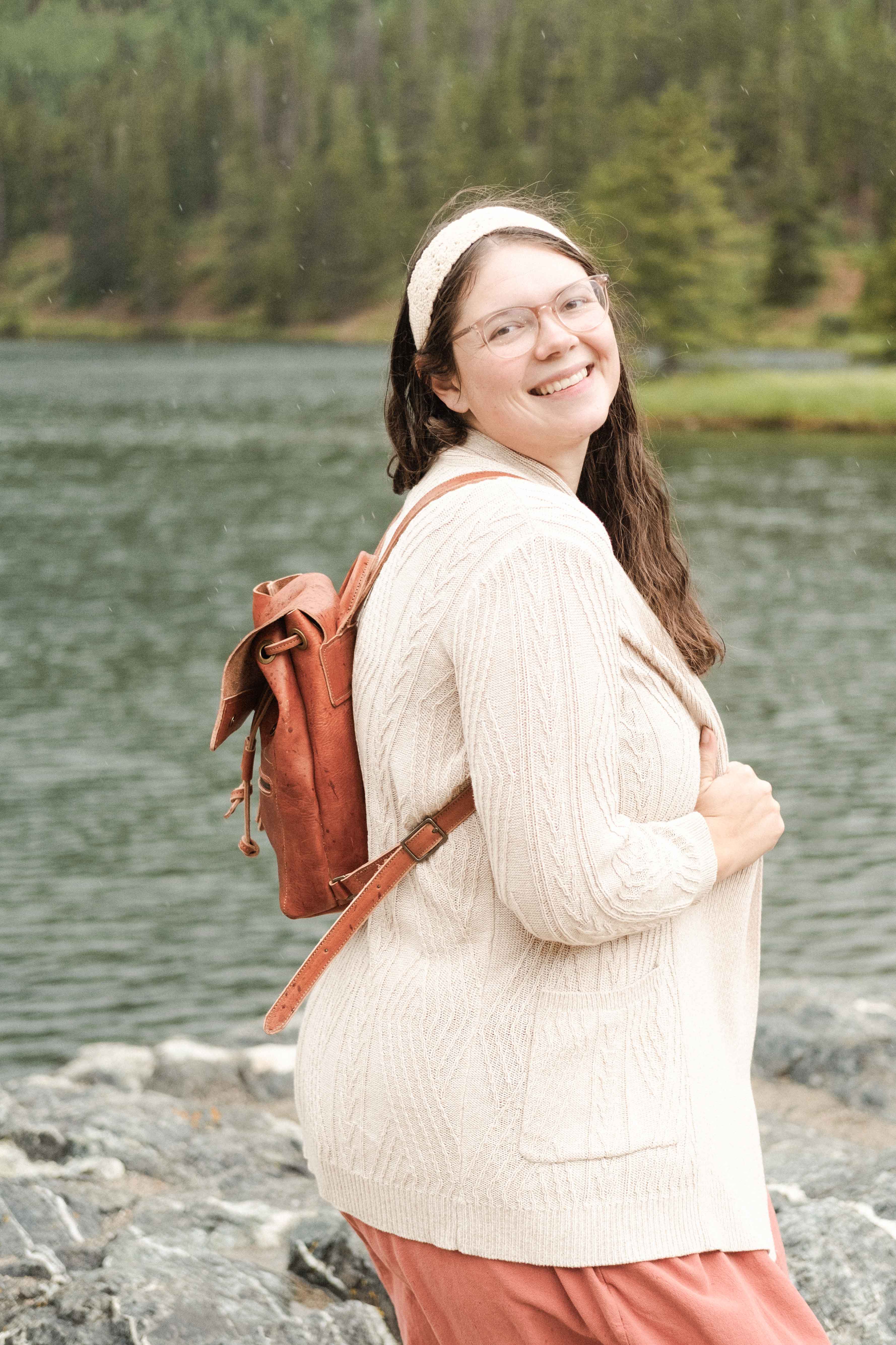 A woman is walking at the shore of mountain lake in Colorado, wearing the small drawstring leather backpack made from non-toxic leather. 