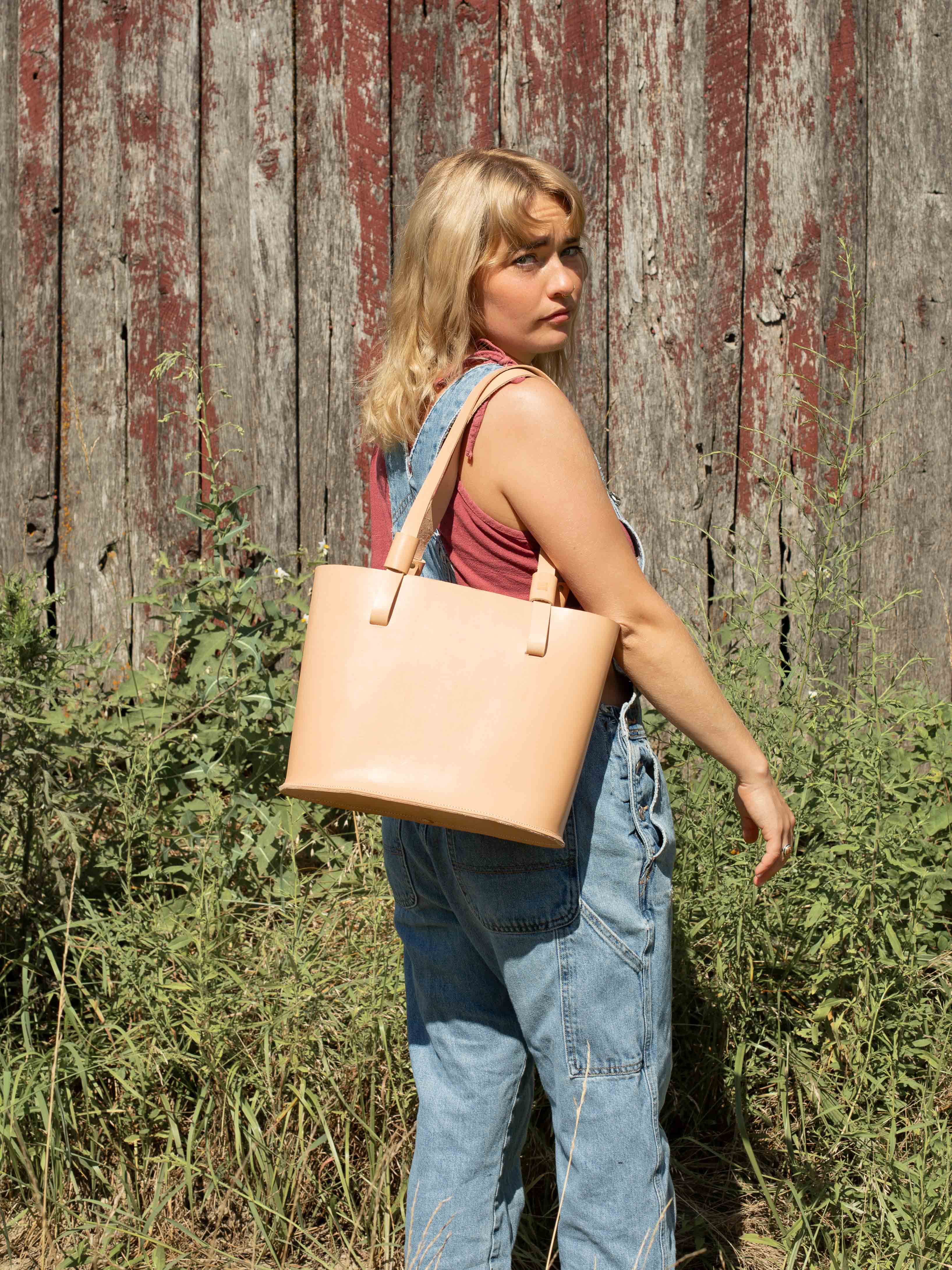 The smaller version of our veg tan tote bag line "The Gatherer" is carried by a model showing the dimensions and look of the sustainable leather shoulder bag. 