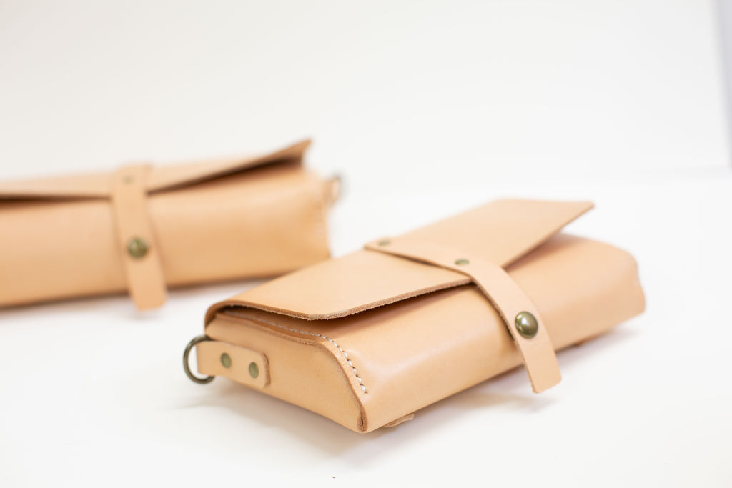 The small handmade leather fanny pack is shown from the size, the large version of the organic leather belt bag is laying further back.