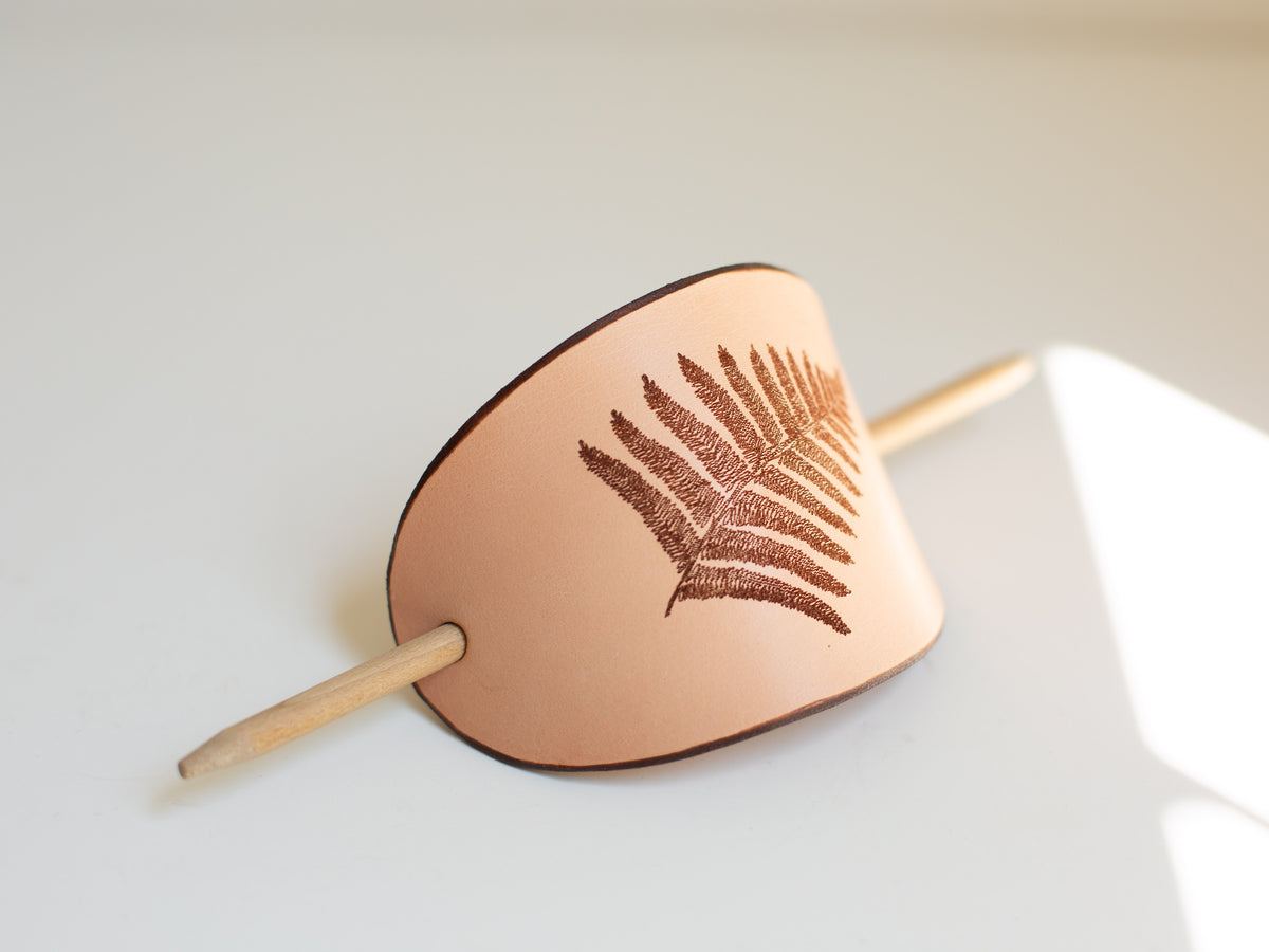 The hair stick barrette is made with organic leather from regenerative farms and has a laser engraved fern on it. 