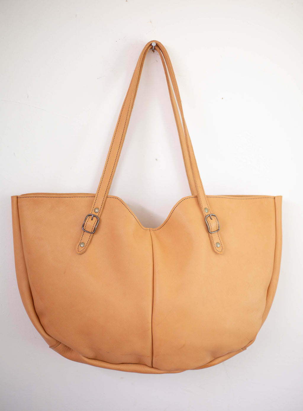 The large tan tote bag, inspired by the seventies, is made from sustainable leather from organic farms. 