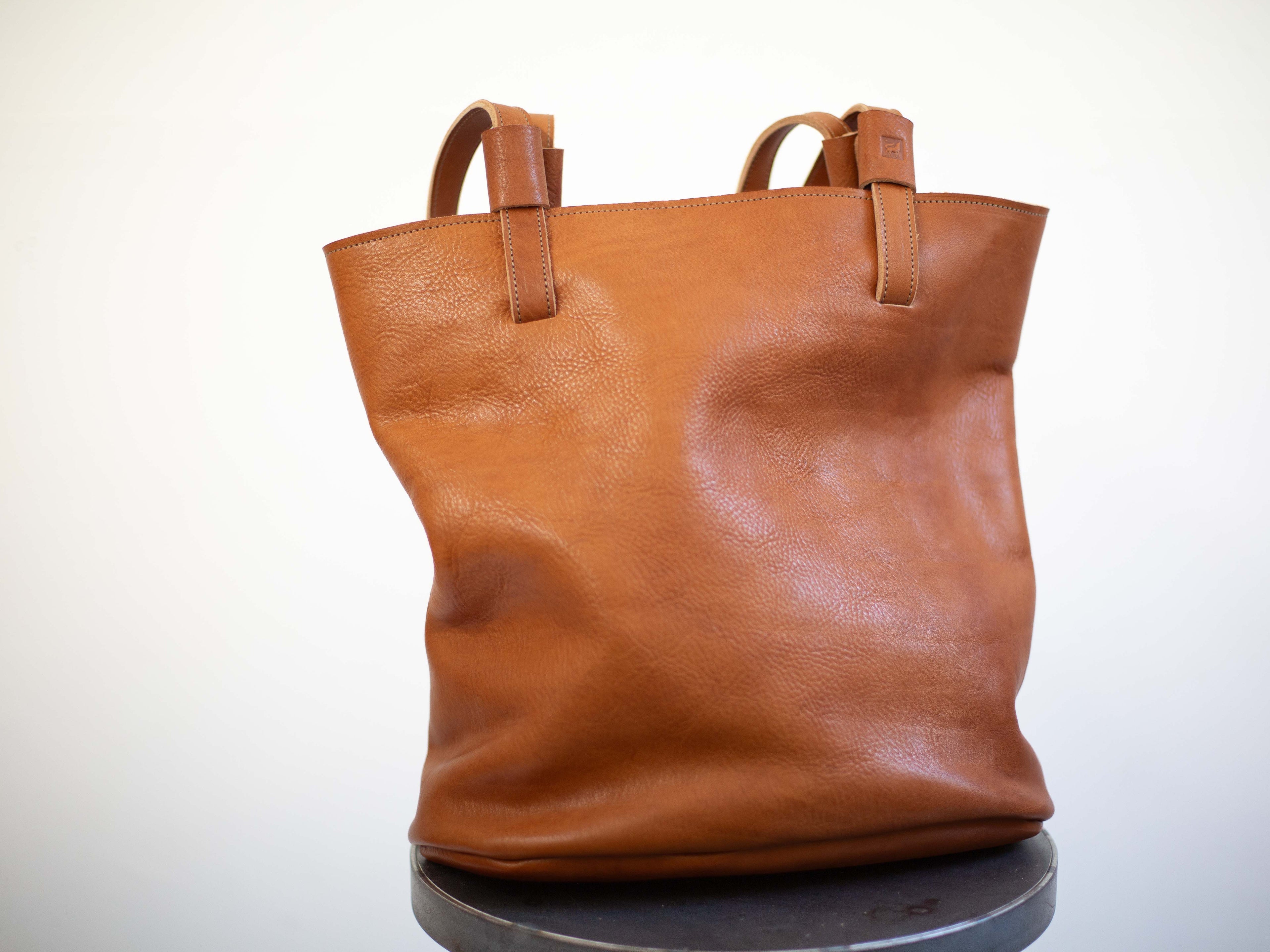The large tote is made with soft, reddish brown organic leather that has a visible grain and texture. The picture shows how valuable the sustainable leather is. 