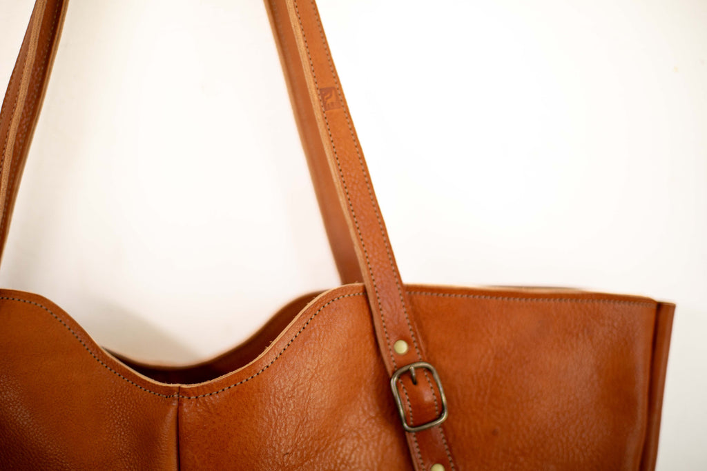 Close-up of brown leather shoulder bag, that shows the detail of the stitching and the natural grain of the sustainably sourced leather from organic farming. 