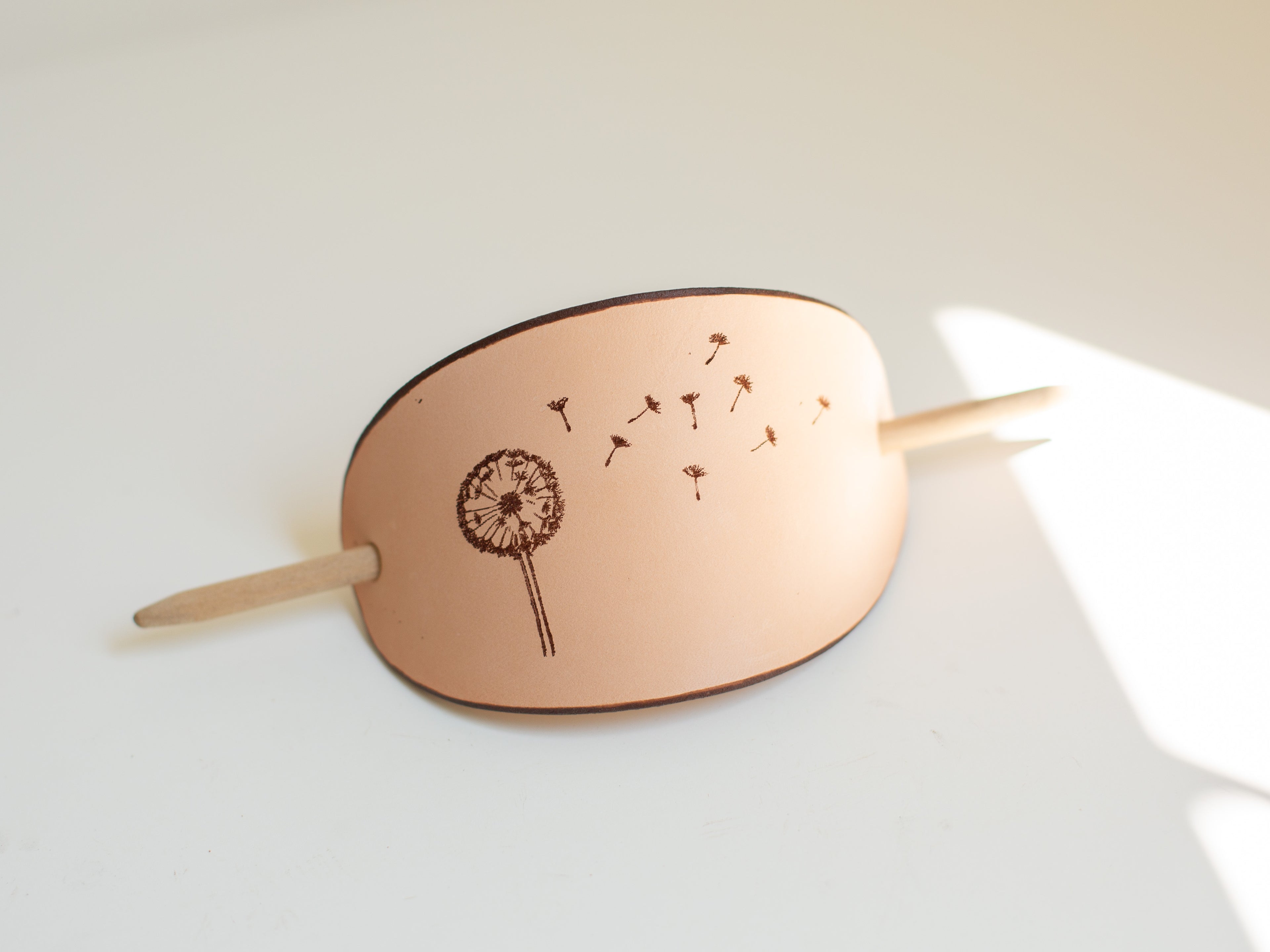 The large leather barrette has a laser engraved dandelion design copied from an original drawing.