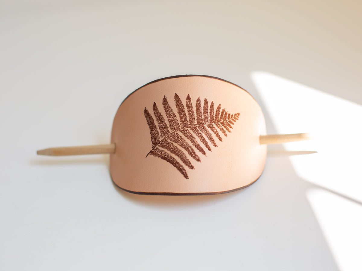 The fern is laser engraved into the leather made with sustainably sourced veg tan leather. 
