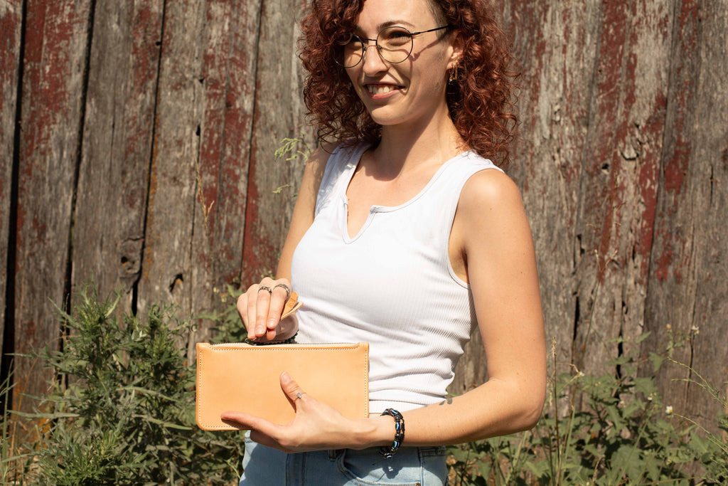 A woman is opening the zipper of the leather tool case. 
