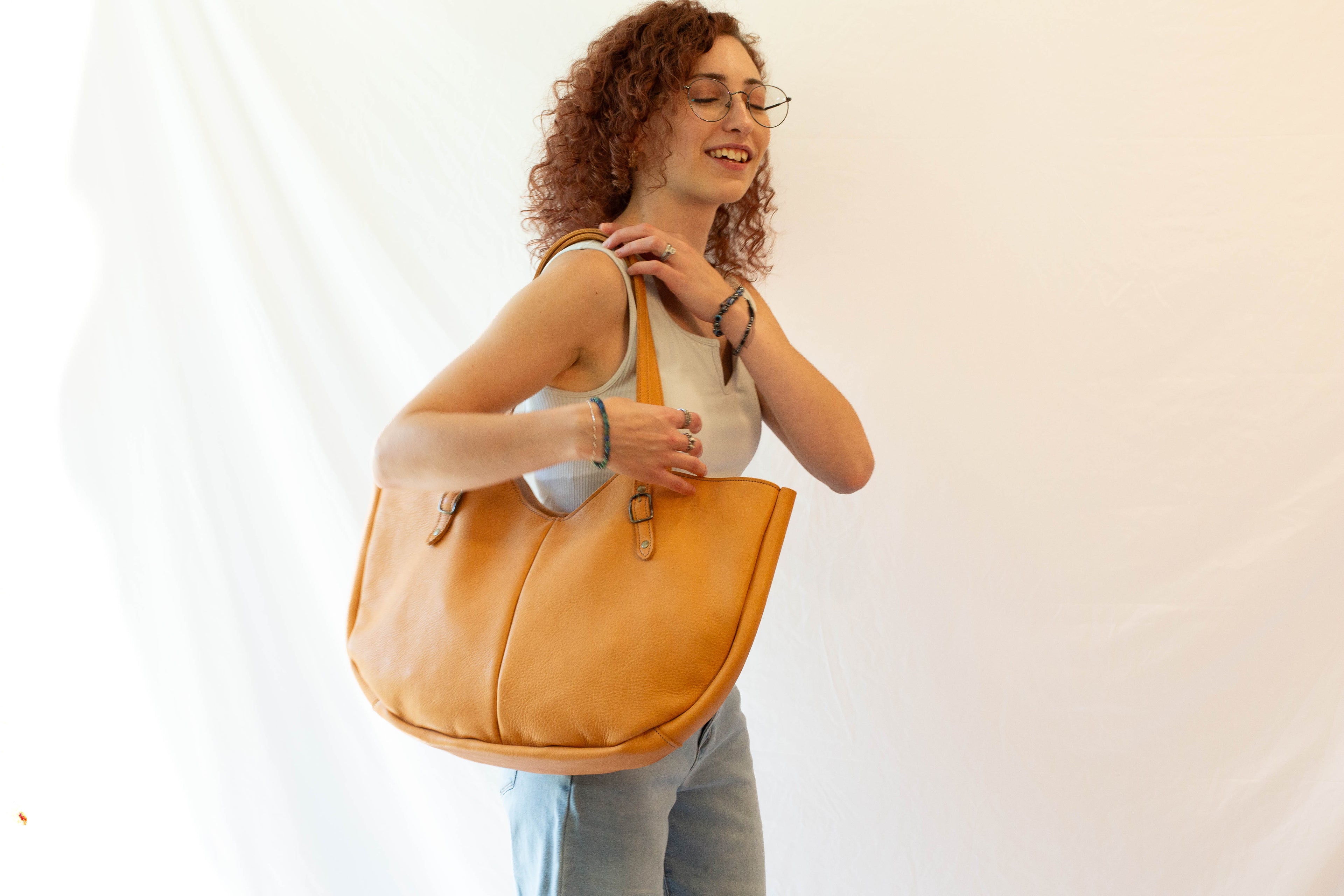 A handmade beige leather shoulder bag, made from ethical leather, is held by a model to show the overall size and look of the bag when in use. 