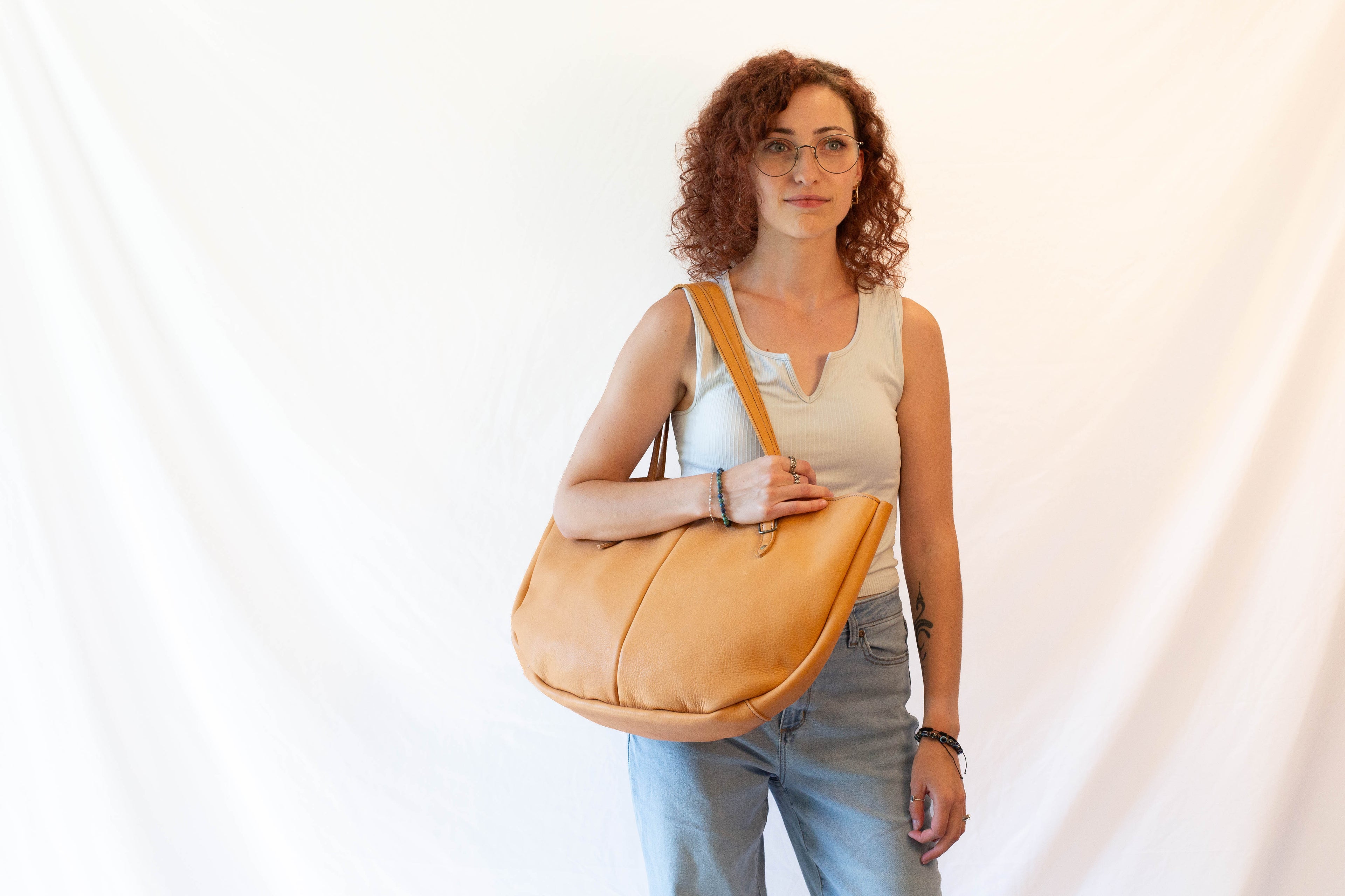 A large leather shoulder bag, made from sustainably sourced leather, is held by a model to show the overall size and look of the bag when in use. 