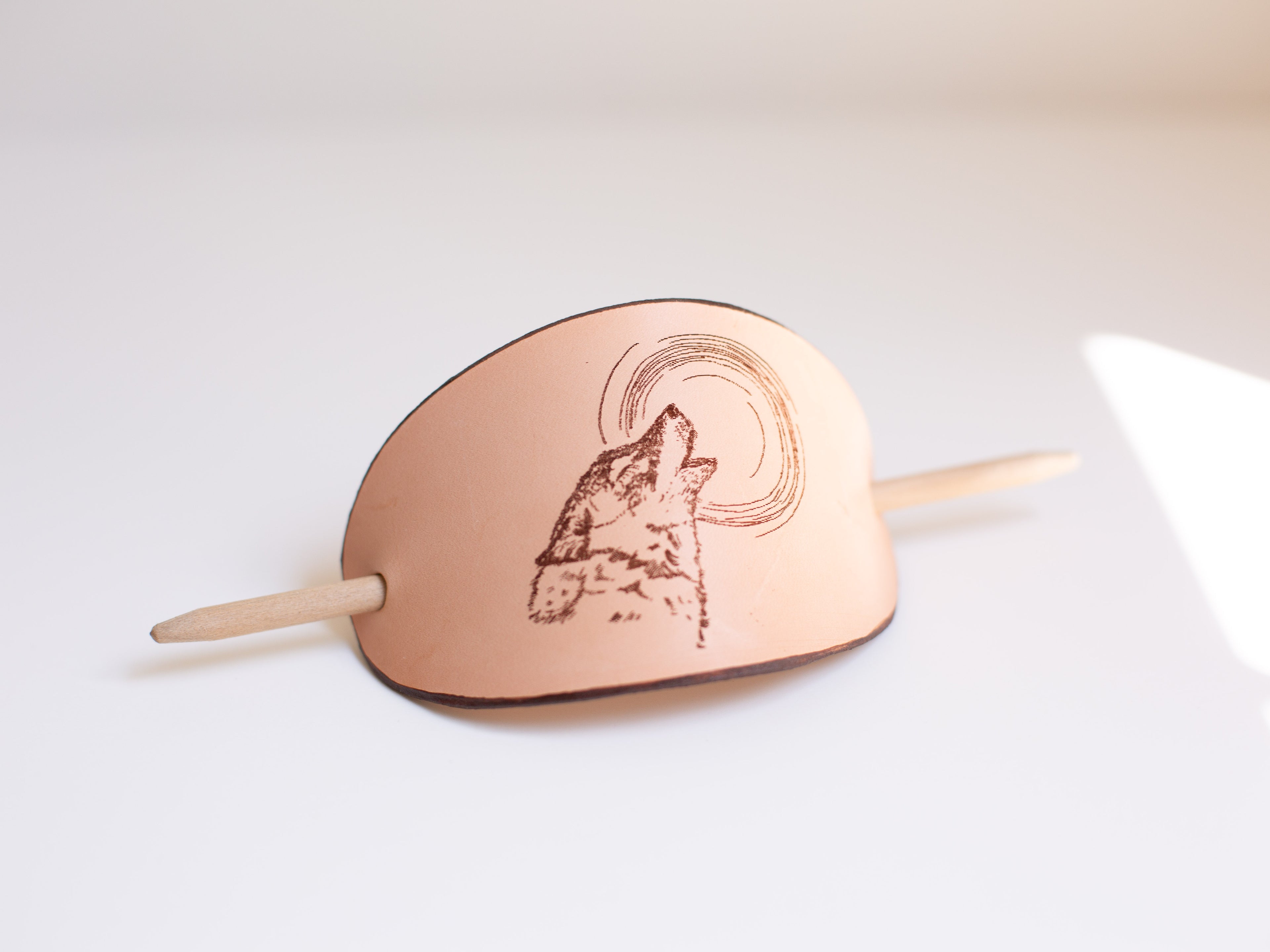 The handmade leather barrette is made with sustainable leather. It has a laser engraving of a wolf howling at the moon. 