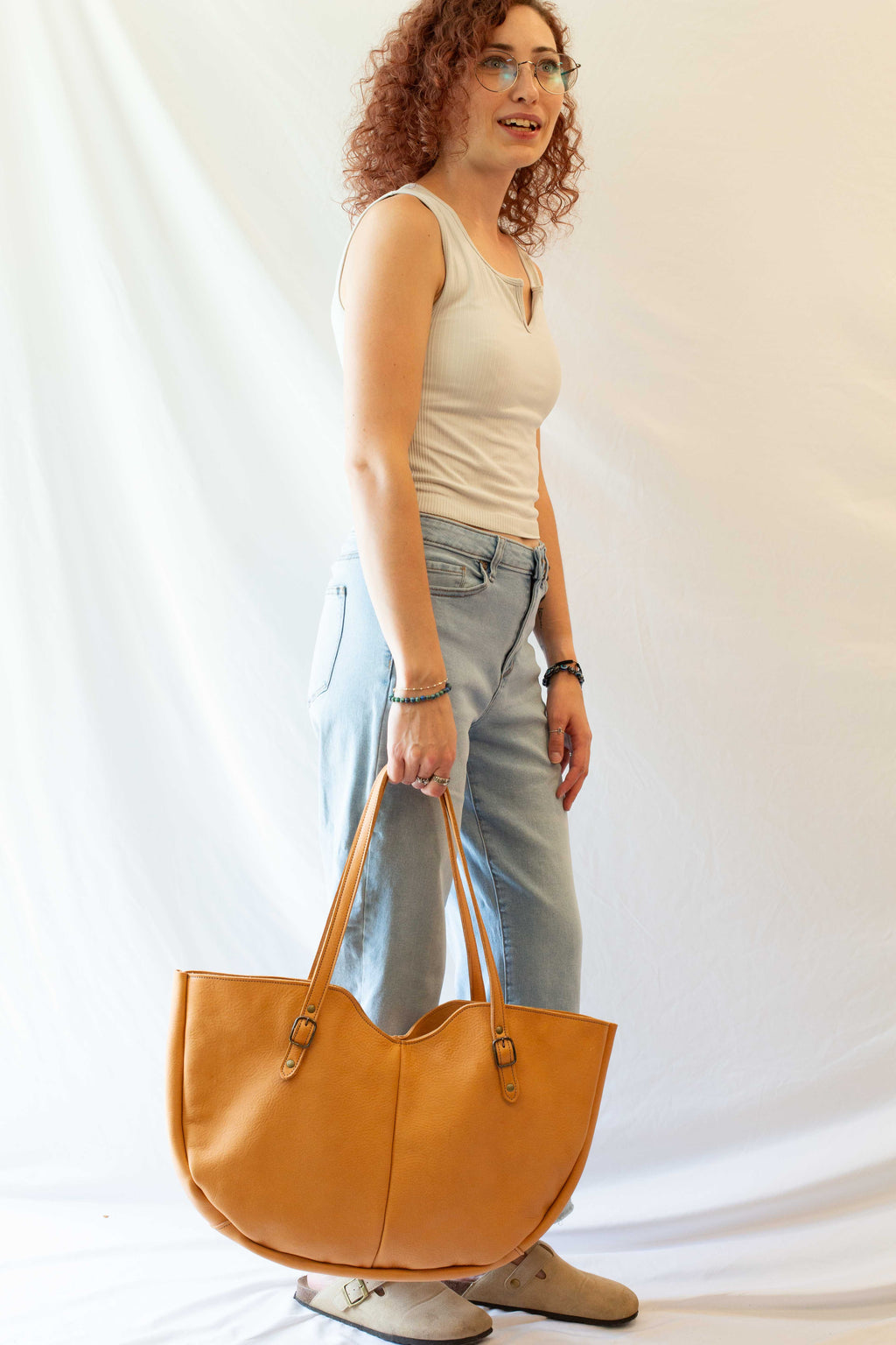 A large leather shoulder bag, made from sustainably sourced leather, is held by a model to show the overall size and look of the bag when in use.